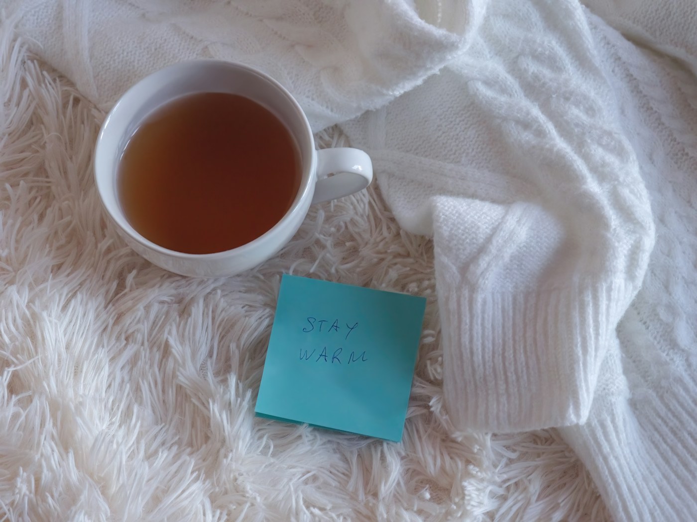 Tasse de thé posée sur un pull en maille blanche et un plaid moelleux